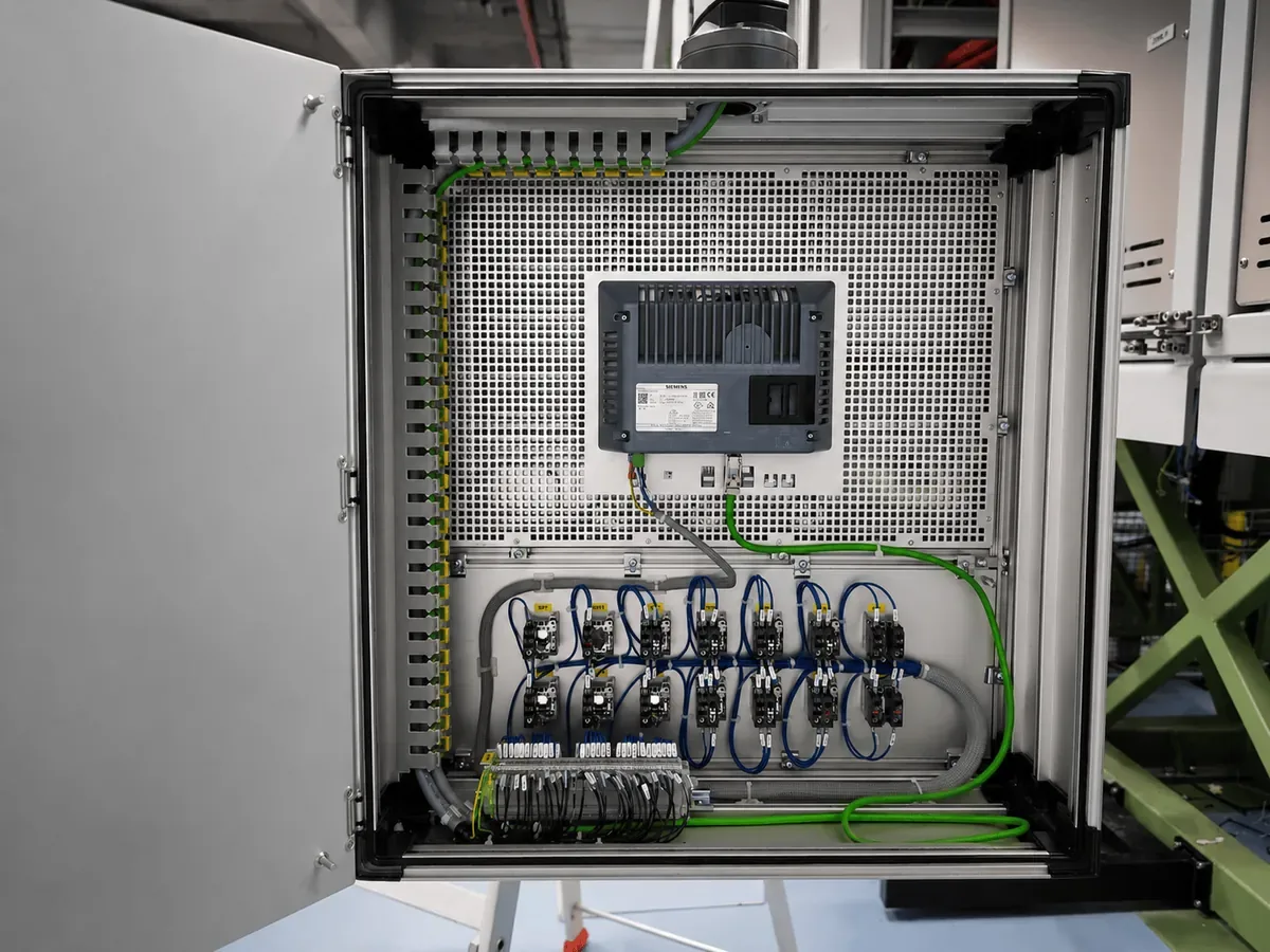 Il retro di un pannello operatore Siemens montato in una cassetta aperta: in alto il pannello con la sua targhetta, il cavo di rete verde che scende verso la morsettiera, sotto due file di relè.