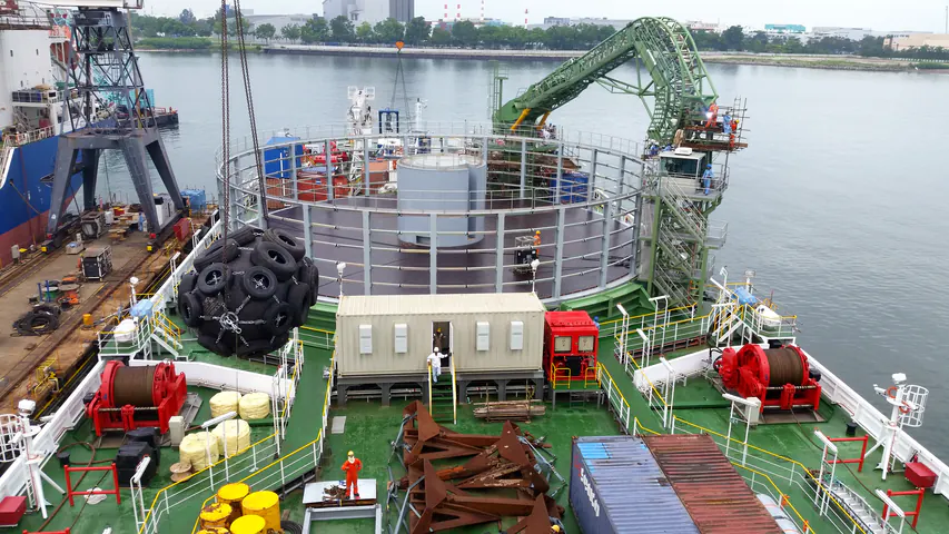 Il ponte della nave Ulisse una settimana dopo: il carousel con la gabbia montata e il nucleo chiuso, la gru di guida verde, i verricelli rossi e un grande parabordo nero appeso alla gru di banchina.