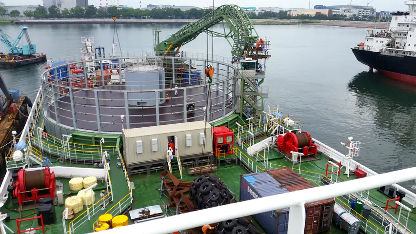 Vista d'insieme del ponte della nave Ulisse: il carousel circolare con il nucleo grigio, la gru di guida verde ad arco, la cabina di comando sulla torre e i verricelli rossi.