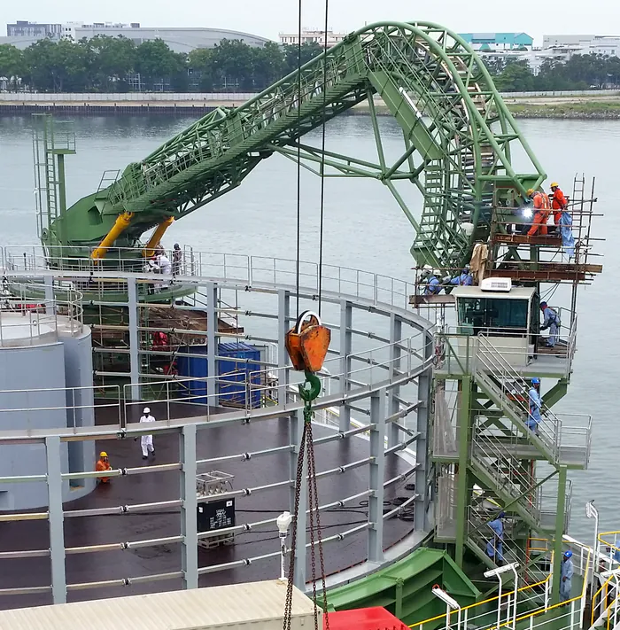 La gru di guida verde ad arco sopra il carousel, con i tecnici al lavoro sulla torre della cabina.